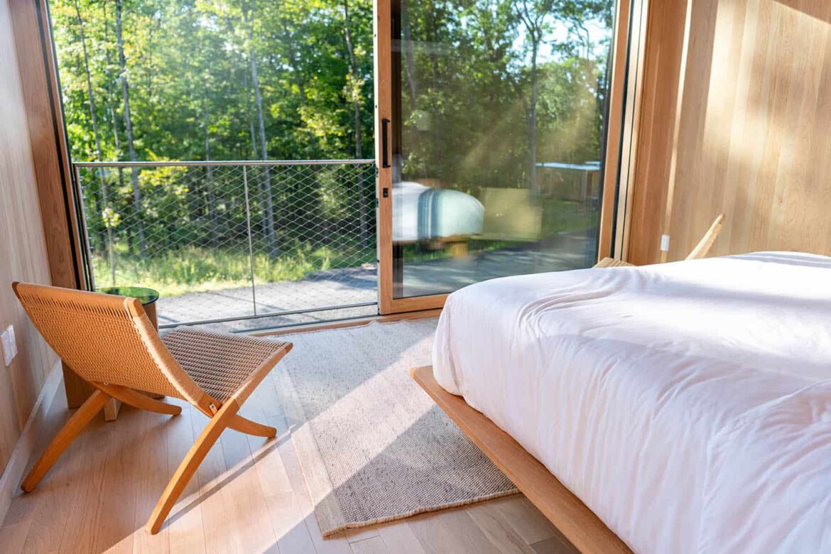 Blick aus einem Schlafzimmer eines Tiny Houses in Bayern, in dem man Urlaub machen kann, bei Sonnenschein auf einen Wald.