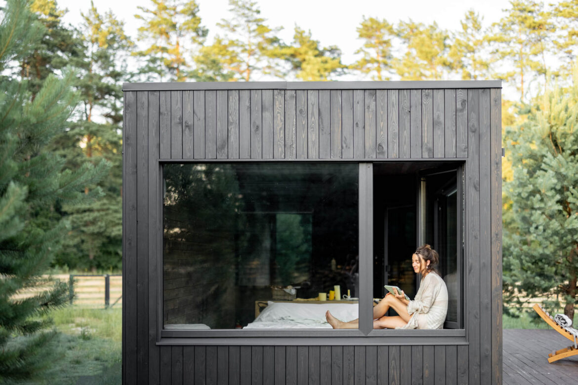 Frau sitzt im Fenster eines Tiny House, welches 50 qm groß ist, und genießt die Natur