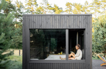 Frau sitzt im Fenster eines Tiny House, welches 50 qm groß ist, und genießt die Natur
