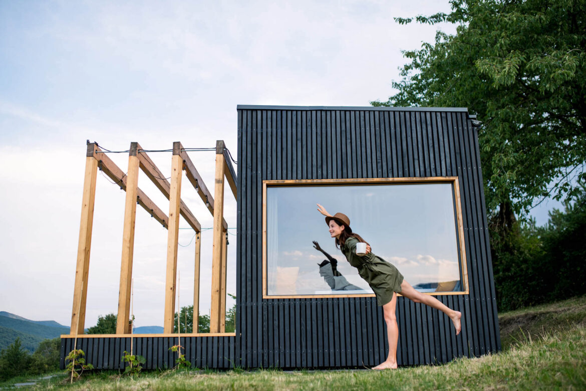 Junge Frau im Freien direkt vor dem Fenster eines Tiny Houses von Tchibo