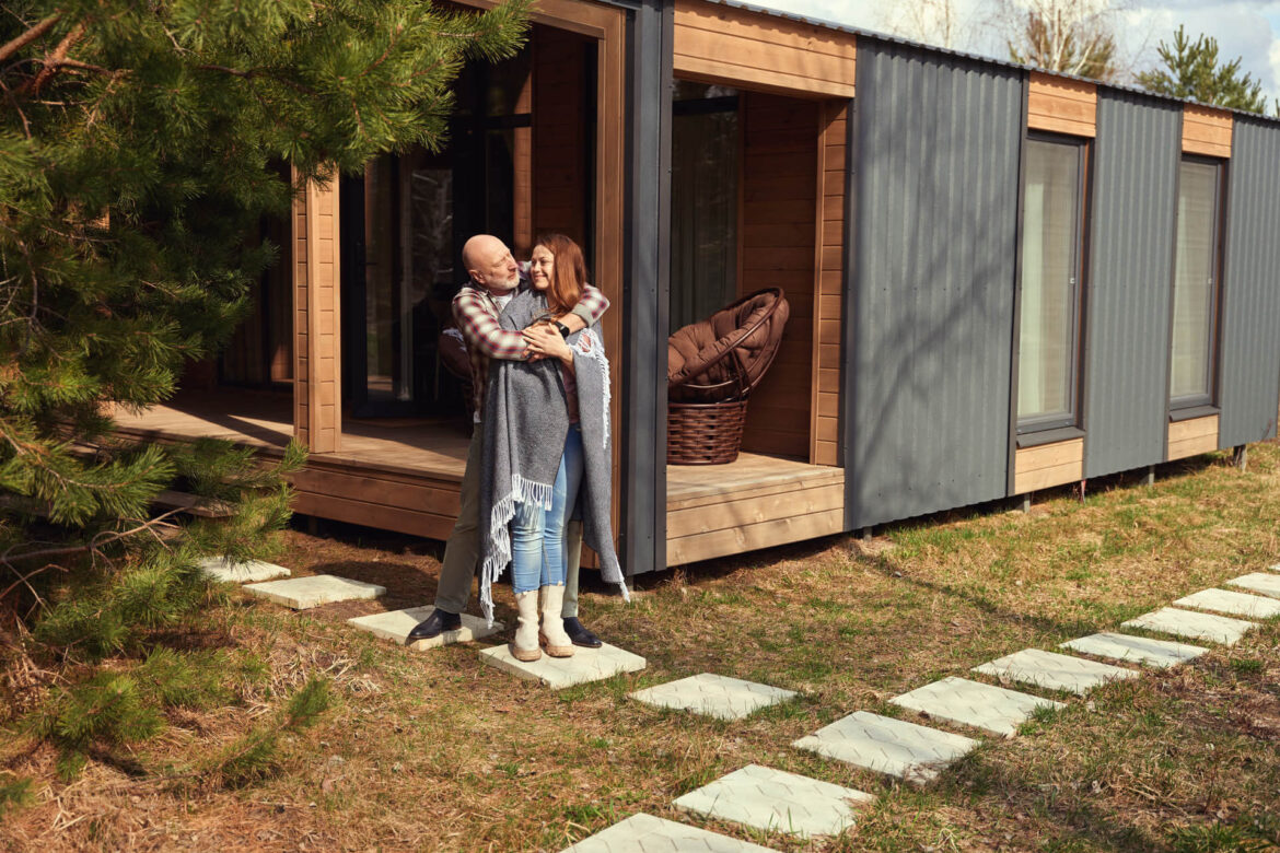 Liebender Ehemann umarmt seine glückliche Frau im Freien vor einem Tiny House,welches 70 qm groß ist, in Hessen.