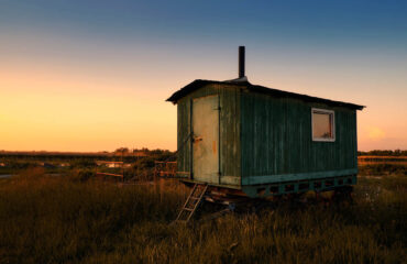 alter und gebrauchter Wohnwagen auf einem Feld in der Landschaft bei Sonnenuntergang