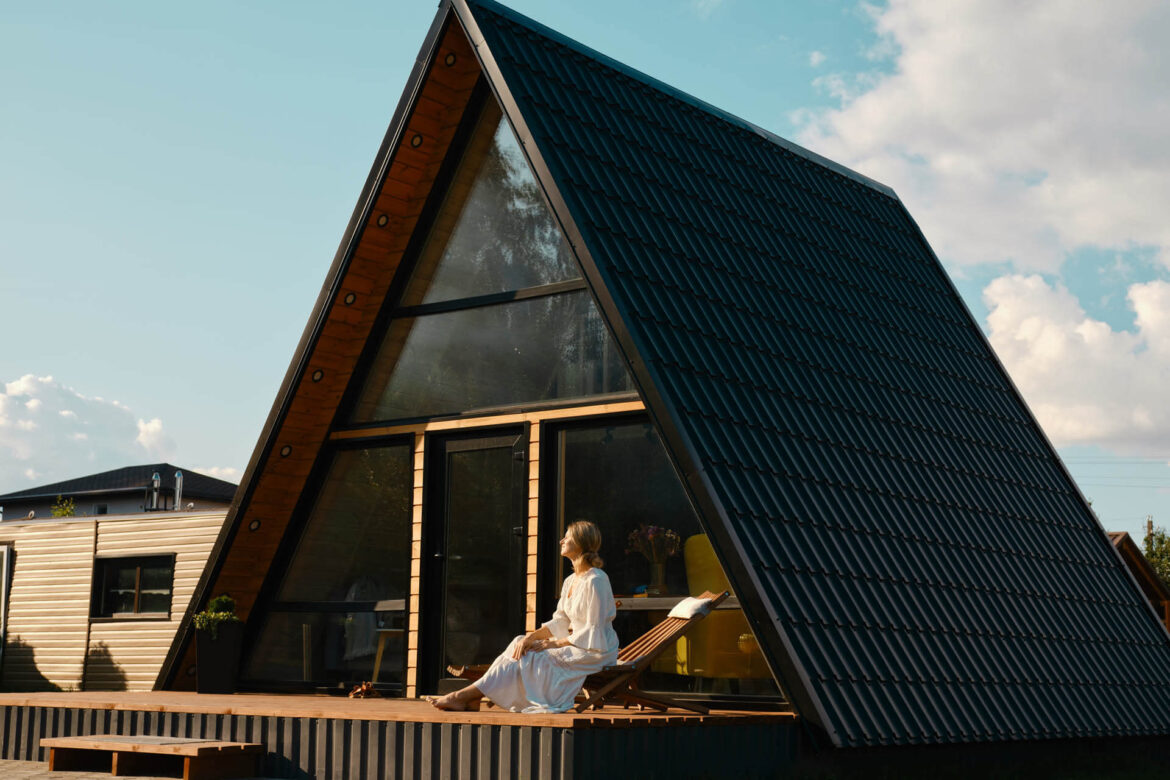 Barfuß Frau in langem Baumwoll-Sonnenkleid ruht auf der Terasse ihres dauerhaft gemieteten Tiny House