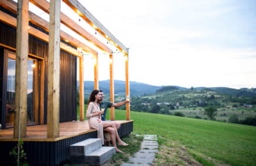 junges Paar mit Wein im Freien auf der Terasse eines Tiny House in Bayern auf einen Privatgrundstück